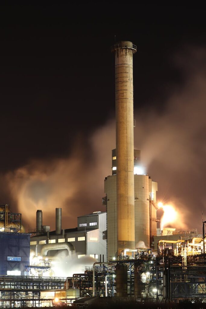 A nighttime view of an industrial factory with smokestacks emitting smoke, highlighting energy production and pollution.